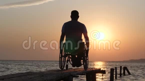 坐在轮椅上的患病男子在夏季旅行时放松举起手中的橙色天空视频的预览图