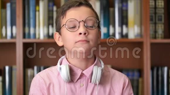 一张可爱的打哈欠的小学生站在图书馆书架附近的肖像视频的预览图