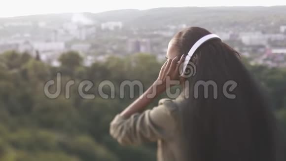 带着棕色长发戴上耳机欣赏城市美景的美国黑人女孩的后景视频的预览图