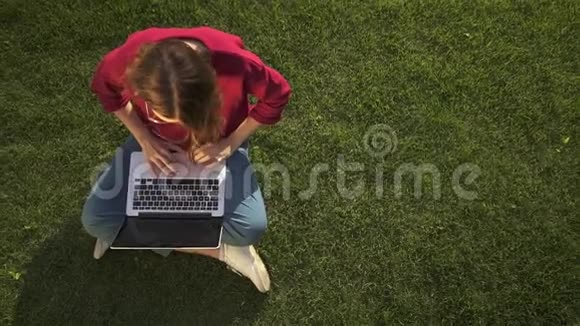 戴眼镜的女人在草地上的笔记本上打字视频的预览图