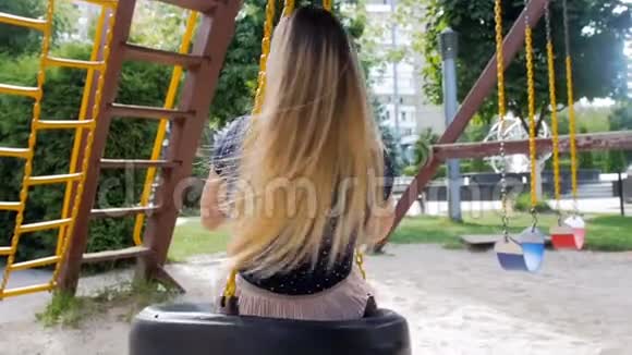 在公园的操场上快乐微笑的年轻女子在秋千上旋转和骑着视频的预览图