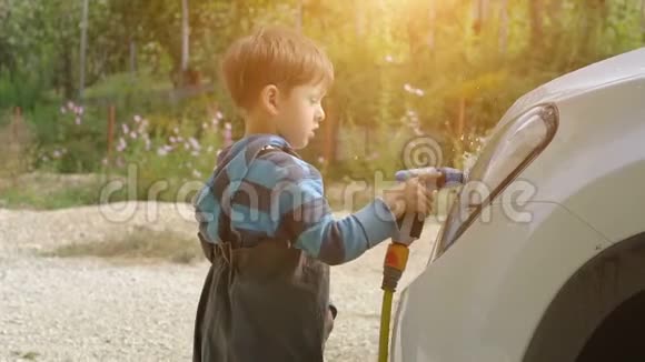 小男孩在花园里洗白色的车夏季视频的预览图