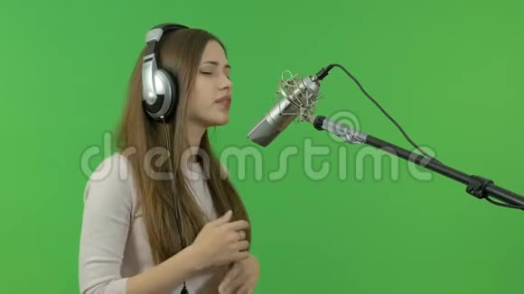 一个年轻女孩正对着录音室的麦克风唱歌特写镜头在绿色的背景上视频的预览图