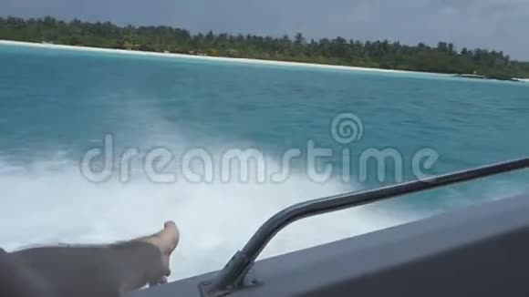 一个人在一艘船上游到一个横跨海洋的热带岛屿上他的手滑在水面上视频的预览图