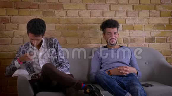 两个年轻的男性朋友坐在舒适的公寓里的沙发上的特写镜头印度男人视频的预览图