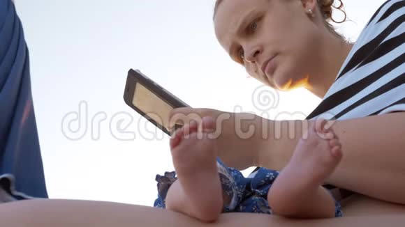 妈妈和熟睡的孩子在海滩上女人用手机视频的预览图