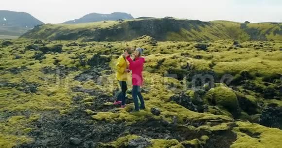 冰岛熔岩场上两名妇女的鸟瞰图直升机飞来飞去的游客在智能手机上自拍照片视频的预览图