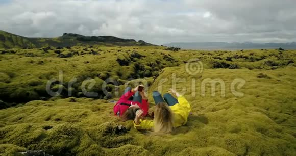 两个女人躺在冰岛柔软的熔岩上的鸟瞰图游客在智能手机上自拍视频的预览图
