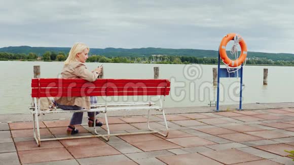 年轻女子坐在一个大湖背景上的长凳上使用手机匈牙利巴拉顿湖视频的预览图