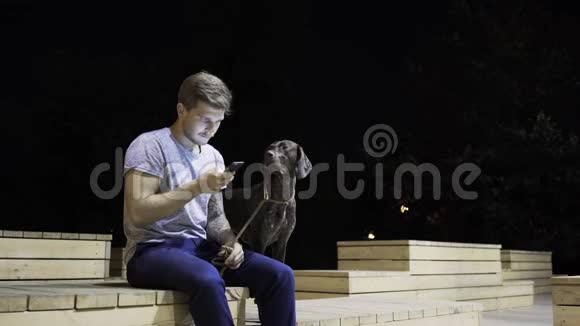 一个金发美女和他的狗在夜间公园的长椅上冲浪视频的预览图