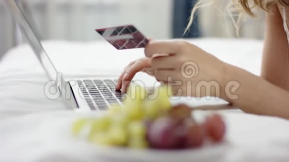 穿着诱惑睡衣的女人躺在床上用笔记本电脑和信用卡通过互联网购物视频的预览图