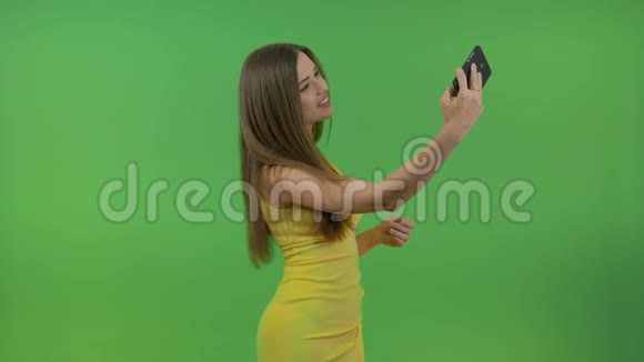 美丽的年轻女孩穿着黄色的裙子在绿色的屏幕上她在智能手机上拍照视频的预览图