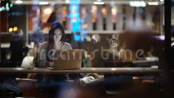 晚上用笔记本电脑看窗户里面的美女女人关上电脑离开咖啡馆视频的预览图