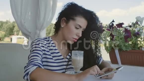 迷人的黑发女郎在夏季露台放松并在电话中输入信息视频的预览图