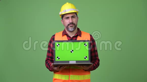 英俊的波斯胡子男建筑工人展示笔记本电脑视频的预览图