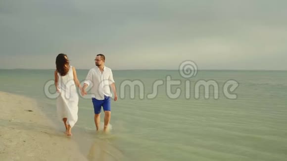 年轻夫妇牵着手沿着海边的水边走着在热带地区度假愉快视频的预览图