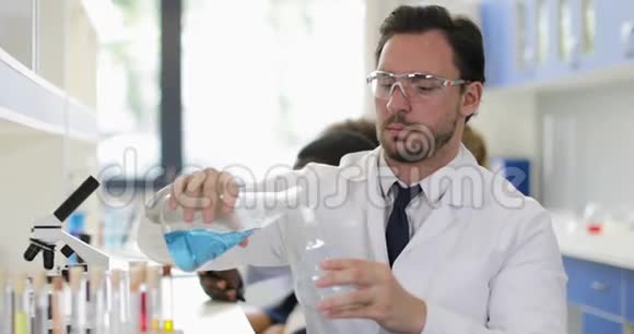 在化学实验室工作时男性科学家在面粉中倒入液体戴上白色外套和防护眼镜视频的预览图