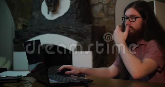 一个留着胡子的年轻人戴着眼镜在黑暗的办公室工作深夜他的脸被屏幕照亮视频的预览图