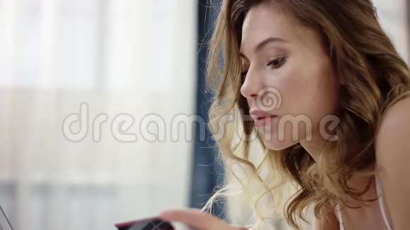 穿着睡衣的女人躺在床上用笔记本电脑和信用卡进行网上购物视频的预览图