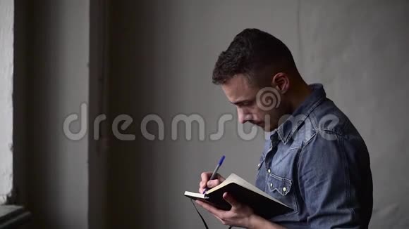 中等镜头的家伙写在笔记本上而站在窗口对面的灰色墙壁视频的预览图