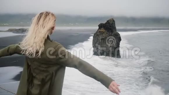 自由年轻美丽的女人站在黑滩的岸边靠近大海看风景视频的预览图