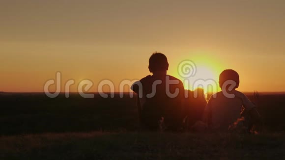两个农村男孩的剪影坐在狗旁边一起欣赏美丽的日落视频的预览图