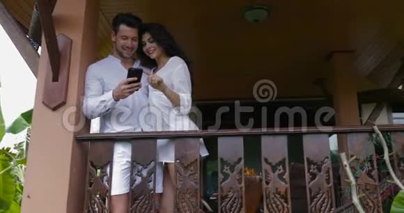 年轻的男女在酒店的阳台上使用手机智能手机幸福的微笑夫妇一起拥抱上网视频的预览图