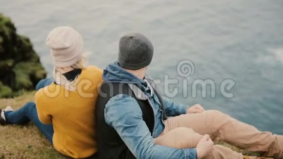 年轻时尚夫妇坐在悬崖边看海欣赏美丽的风景视频的预览图