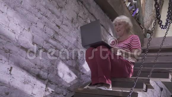 高级妇女坐在楼梯上用可视电话与亲戚交谈视频的预览图