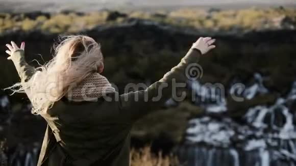 自由后景年轻幸福的女人看着冰岛的巴拉福斯瀑布举起手跳跃着欢乐视频的预览图