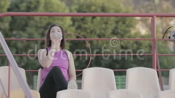 美丽的健身女孩在体育场训练后喝一瓶水视频的预览图