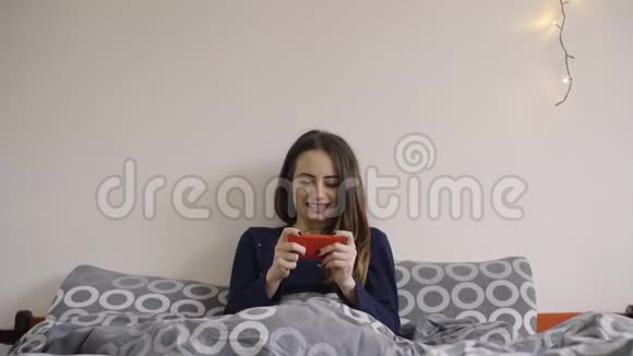 女人在床上开心地玩手机游戏视频的预览图