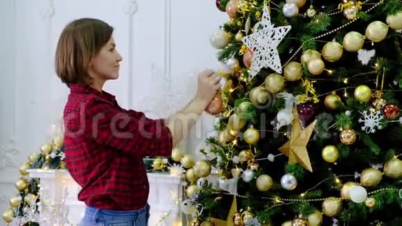 女人在房间里用金色玩具装饰圣诞树视频的预览图