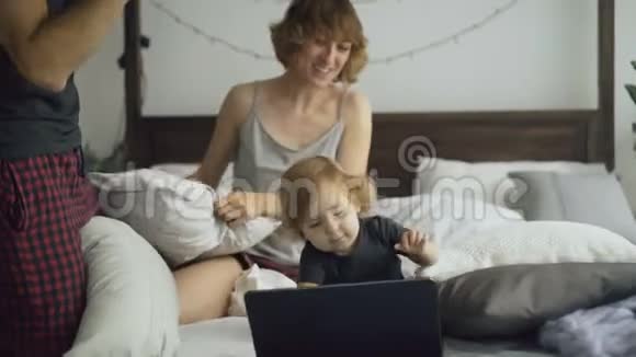 幸福的家庭和小可爱的女儿在家里的床上玩和打枕头视频的预览图