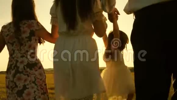 妈妈爸爸和小女儿带着姐姐在阳光下田野里散步快乐的年轻家庭孩子们爸爸和妈妈视频的预览图