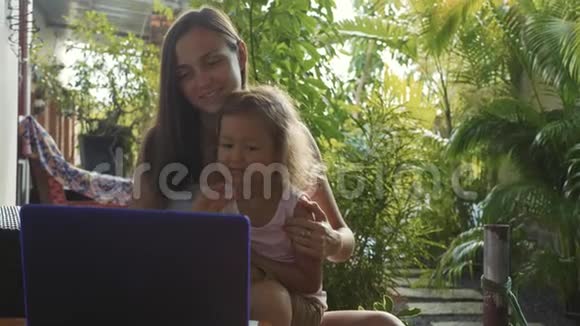 年轻女子带着可爱的小女儿一起用笔记本电脑慢动作视频的预览图