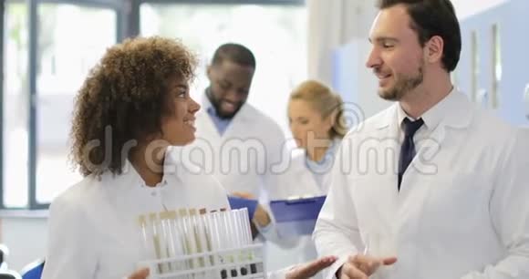 在现代实验室中男性和女性科学家拿着装有化学物质的试管和面罩在一起工作视频的预览图