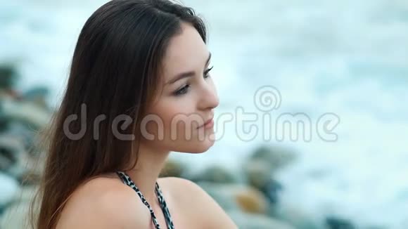 夕阳下坐在碧海背景下的石头上的美丽的女人视频的预览图