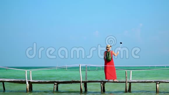 穿红色衣服的女人带着绿色背包在码头上散步旅行者把自己的照片贴在赛尔夫棍子上视频的预览图