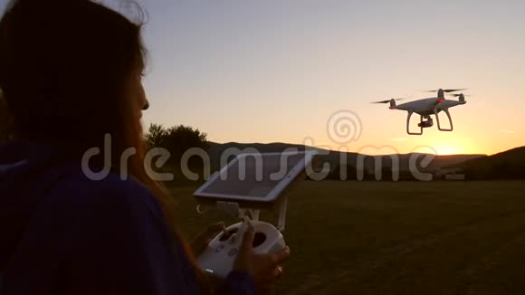 年轻的快乐女孩与远程控制控制四直升机无人机现场在日落高清慢速运动视频的预览图