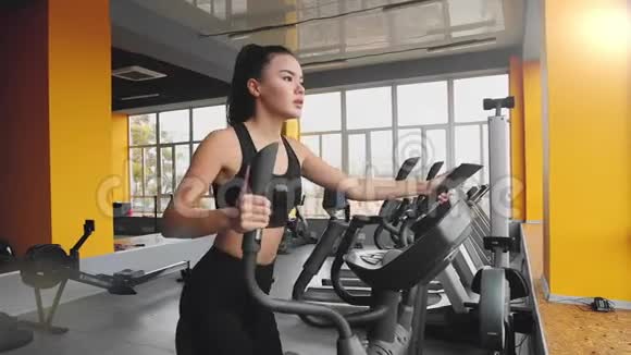 年轻的亚洲女孩在健身房的椭圆教练上做运动视频的预览图