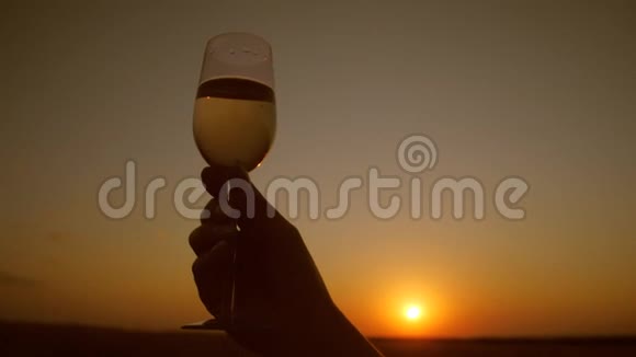 在美丽的夕阳背景下手捧一杯起泡葡萄酒视频的预览图