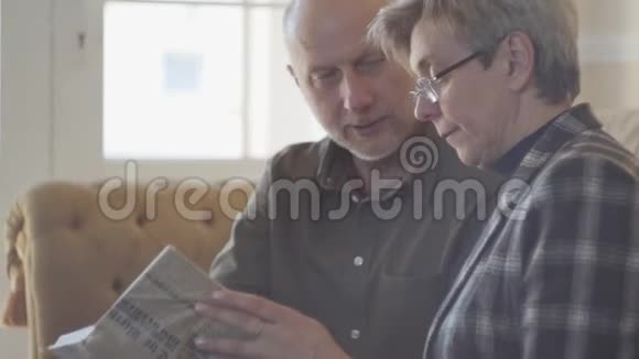 成熟的夫妻男人和女人坐在沙发上拿着一本书互相交谈和微笑家庭视频的预览图