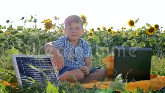 孩子在向日葵的背景场上在太阳能电池附近展示手势和微笑男孩使用太阳能视频的预览图