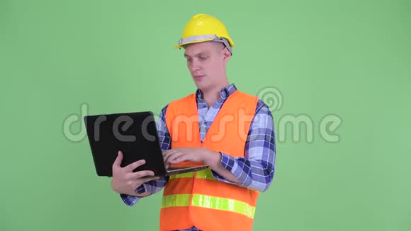 快乐的年轻人建筑工人一边思考一边使用笔记本电脑视频的预览图