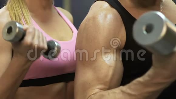 男人和女人通过举起哑铃在健身房锻炼同时弯曲手臂视频的预览图