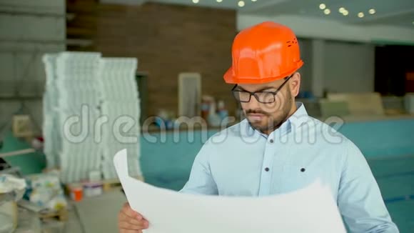 建筑工程师或建筑师戴橙色头盔在建筑背景上有施工计划视频的预览图