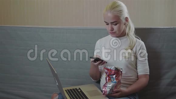 晚上在家看电影的女孩在家吃薯片带手机笔记本电脑金发模特视频的预览图