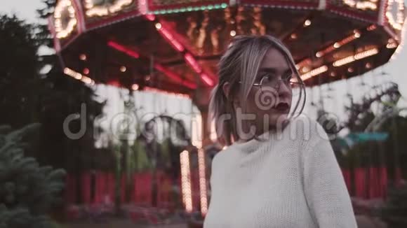 戴眼镜的年轻女孩站在游乐园的旋转木马附近视频的预览图