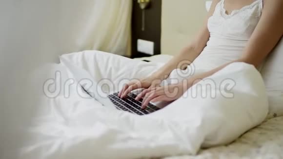 年轻可爱的女人穿着睡衣在床上的笔记本电脑键盘上打字视频的预览图